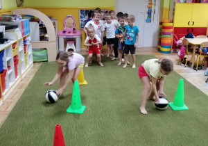Dzieci toczą piłkę lekarską pomiędzy pachołkami